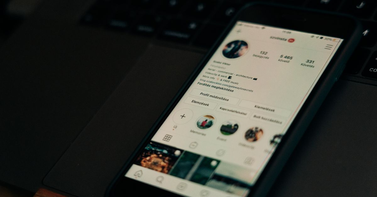 Close-up of smartphone showing a social media profile screen next to a laptop.